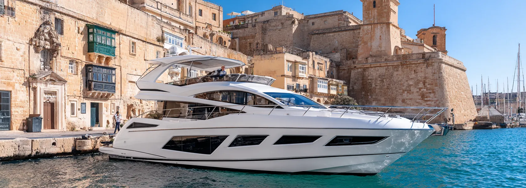A white motor yacht alongside a limestone quay below the bastions in Malta, in bright sunshine